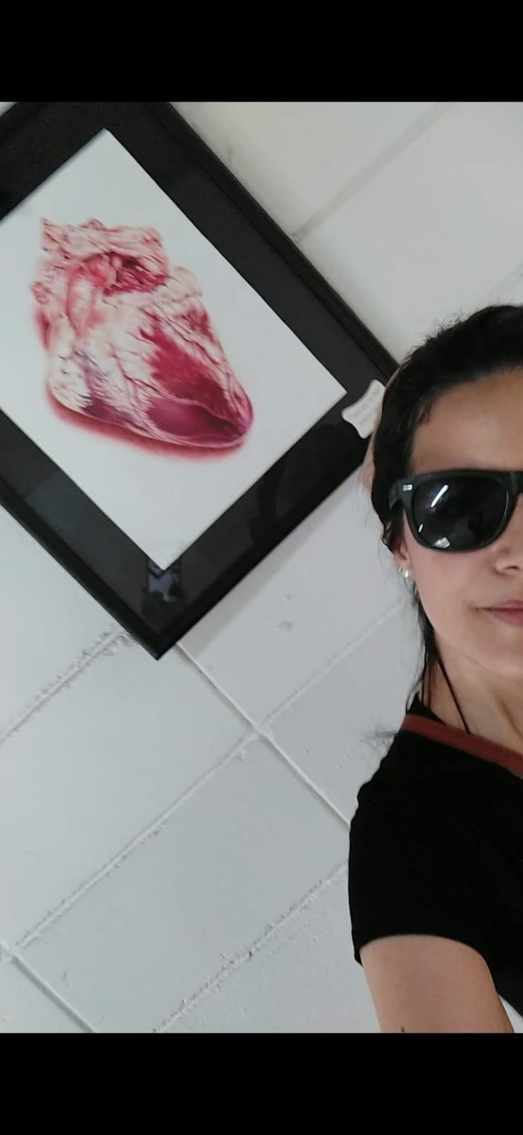 Cíntia Cris beside a framed drawing at the exhibition